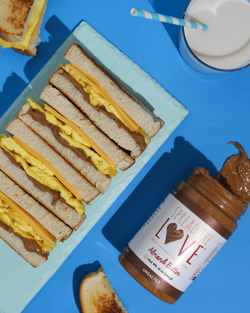 Tray of Almond Butter Gouda Omelette Sandwiches and a jar of Spread The Love Almond Butter with a glass of milk 