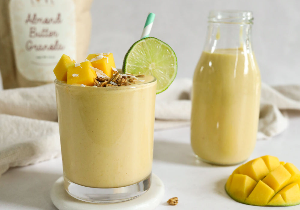 A glass of Mango Cream Smoothie topped with mango, granola, and lime 