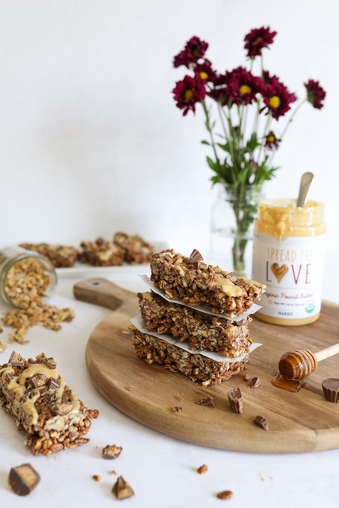 Wood board with peanut butter cup granola bars and Spread The Love Peanut Butter jar