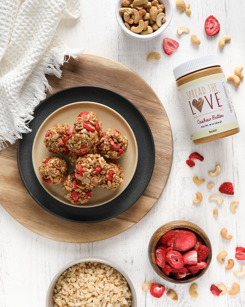 Bowl with Strawberry Cashew Crunch Bites surrounded by Cashew Butter Jar, Cashews, and Strawberries