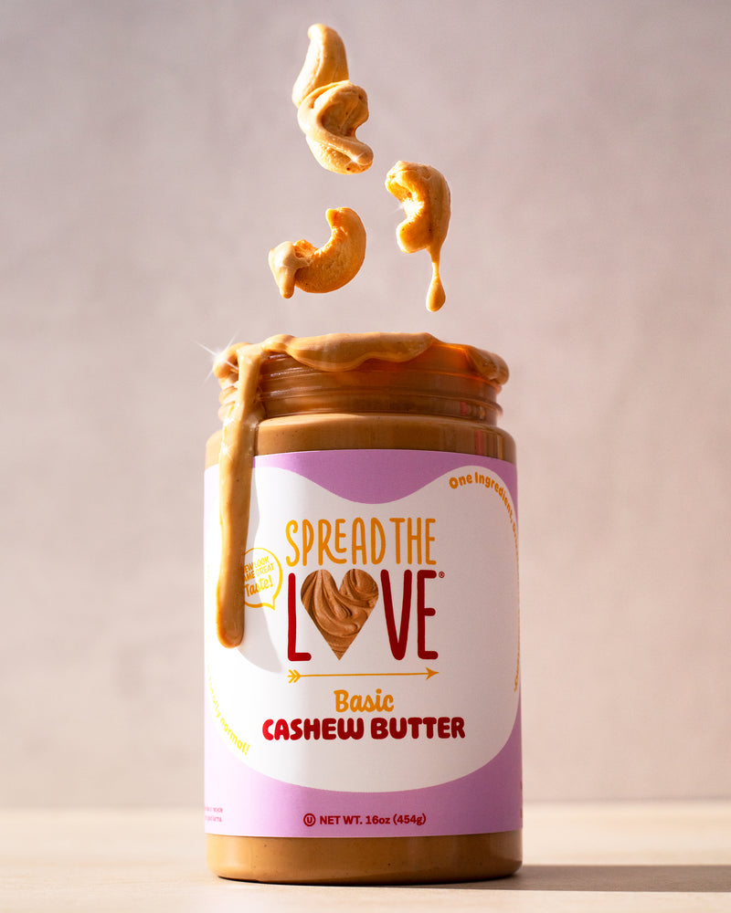 Jar of Spread The Love Basic Cashew Butter with cashews falling into it