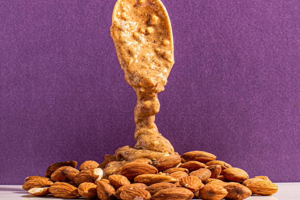 Almond butter drizzling on pile of almonds.