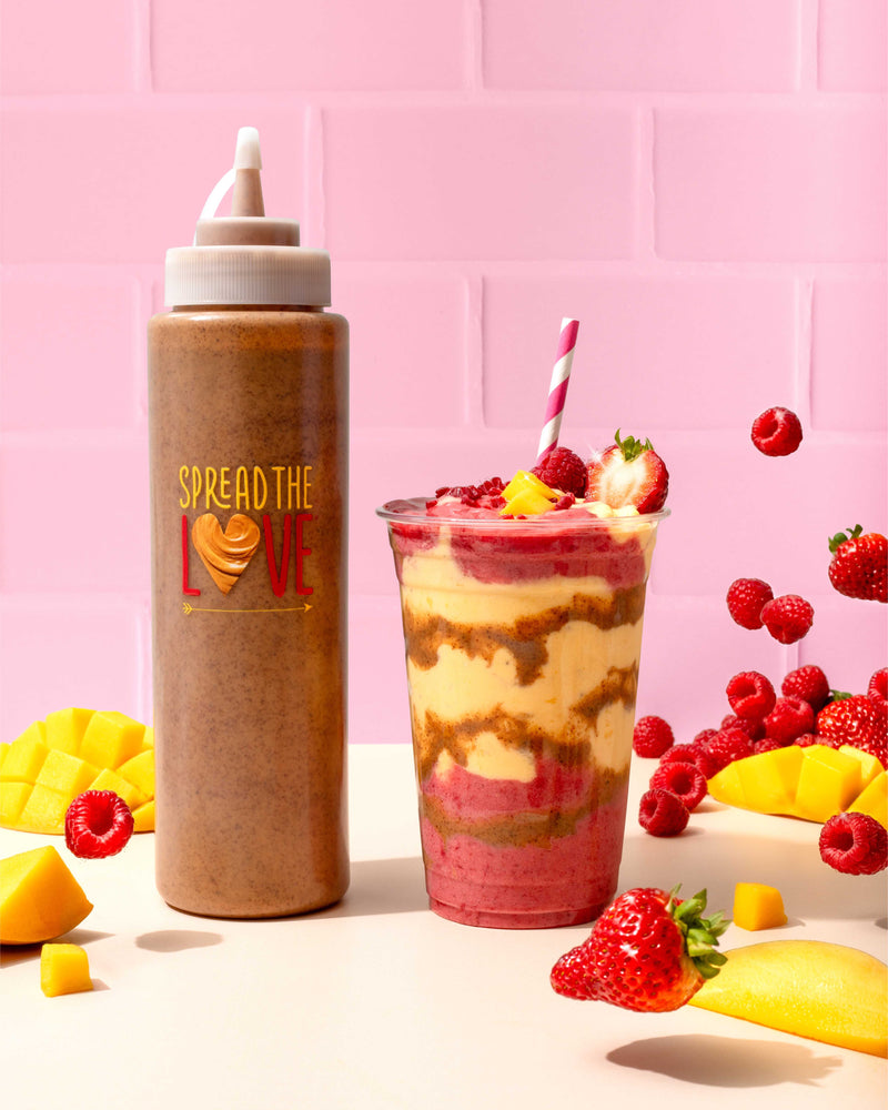 Berry Mango Antioxidant Smoothie next to Spread The Love Squeeze Bottle with Almond Butter surrounded by fruit