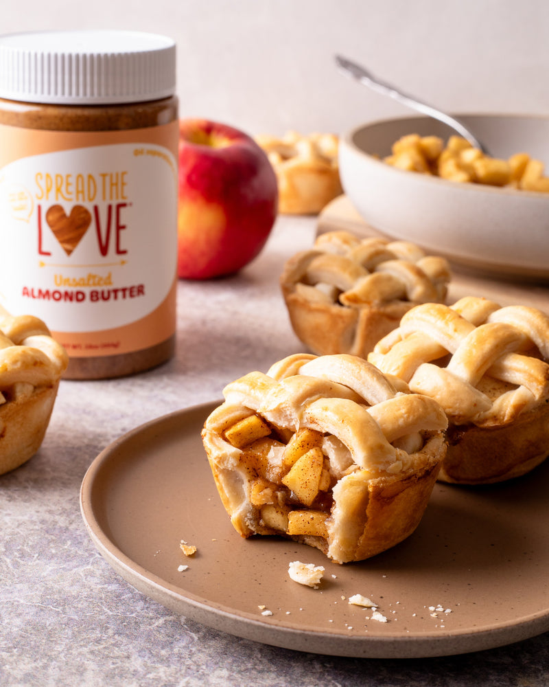 Plate of mini apple pies with almond butter drizzle and Spread The Love Almond Butter jar in the back