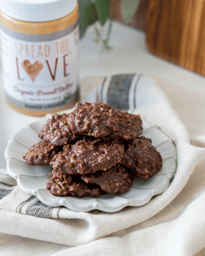 Plate of No Bake Peanut Butter Cocoa Cookies with Spread The Love Peanut Butter in the background