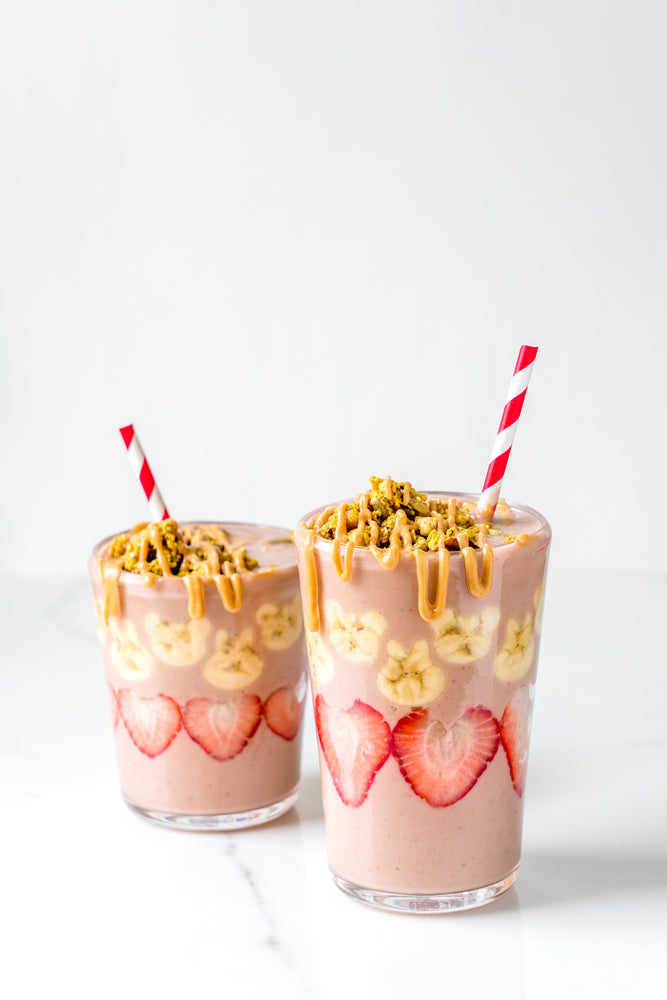 2 cups of the Pretty in Peanut Butter Smoothie topped with granola and Peanut Butter Drizzle