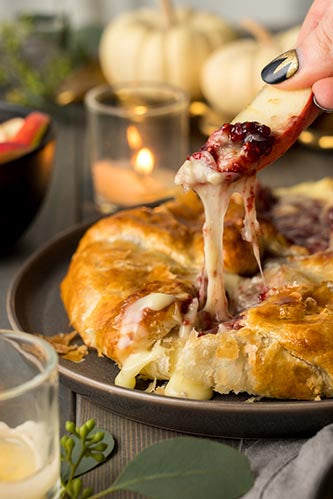 Someone sipping apple slice into baked brie en croute with raspberry jam 