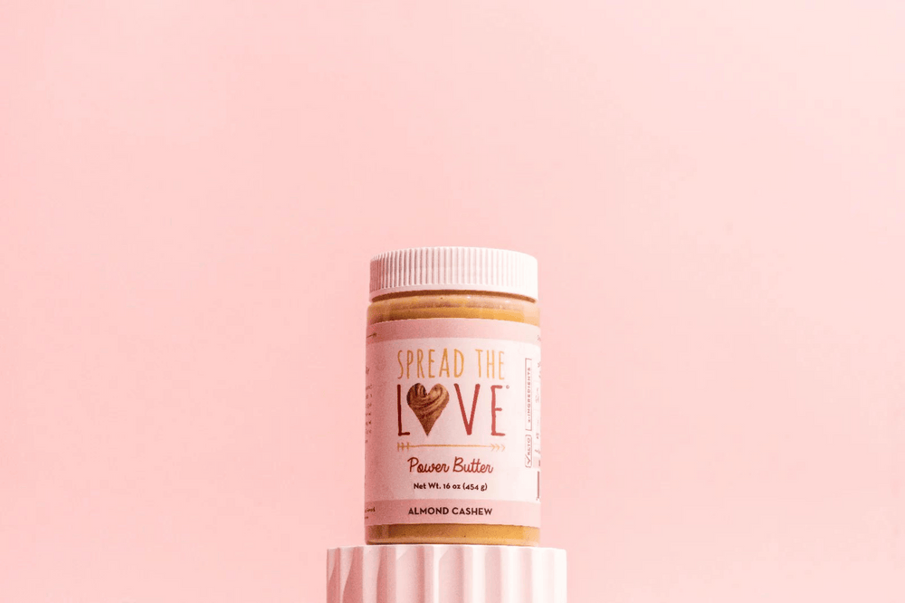 Almond Cashew Power Butter Jar on pedestal with pink background.