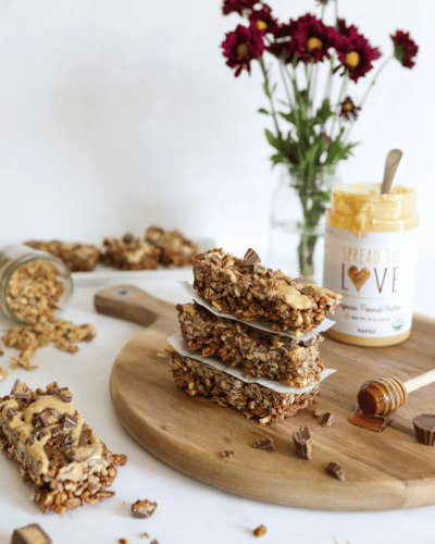 Wood board with peanut butter cup granola bars and Spread The Love Peanut Butter jar