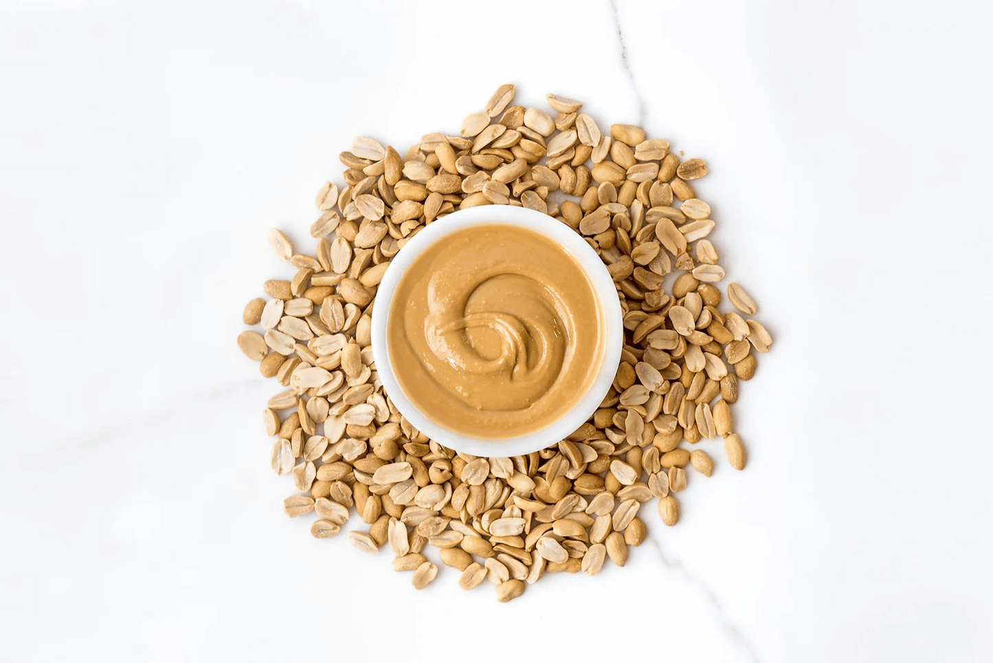 Bowl of Peanut Butter surrounded by peanuts.