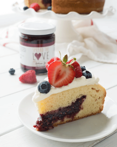 Plate with a slice of Raspberry Jam Cake on it topped with strawberries and blueberries