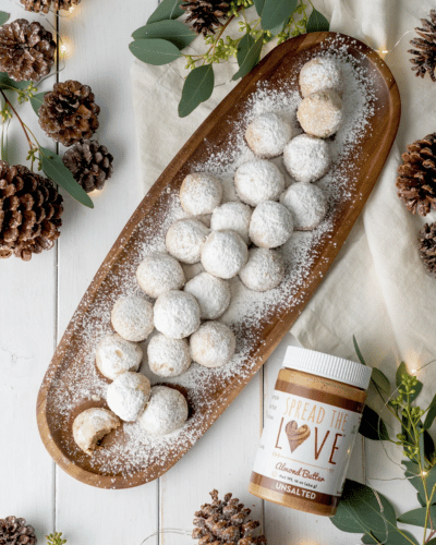 Plate full of spiced almond butter snowball cookies surrounded by pinecones and leaves