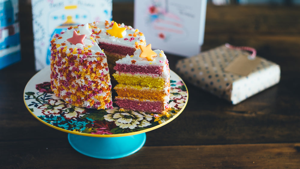 A colorful layered cake with star decorations on a floral plate, with a gift in the background
