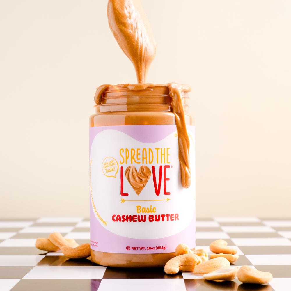 
                  
                    Load image into Gallery viewer, A jar of Spread The Love Basic Cashew Butter with spoon drizzle and cashews on the side.
                  
                