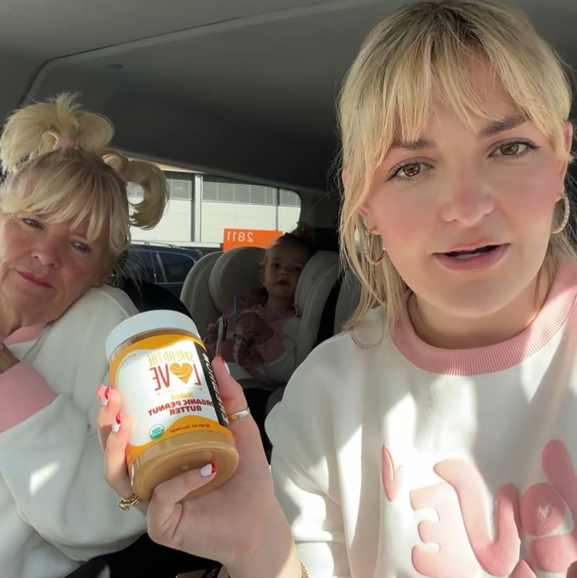 Two women in a car, one holding a jar of peanut butter.