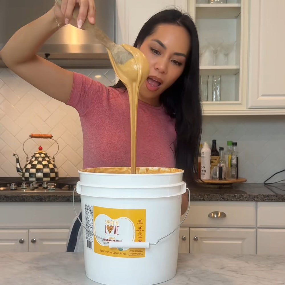 Woman pouring a thick yellow substance from a spoon into a white bucket labeled 'Love' in a kitchen.