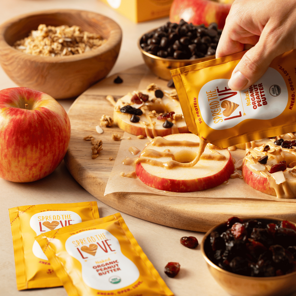 
                  
                    Load image into Gallery viewer, Hand pouring a packet of Spread The Love Peanut Butter onto apple slices 
                  
                