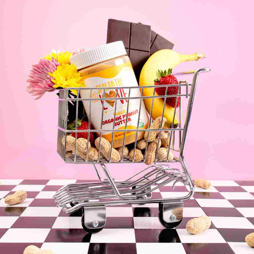 Spread The Love Peanut Butter jar in tiny grocery cart with pink background and checkered floor