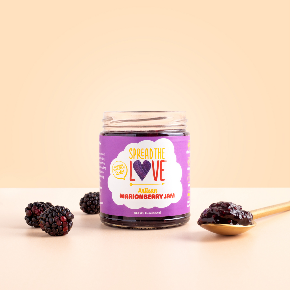 
                  
                    Load image into Gallery viewer, Spread The Love Marionberry Artisan Jam on counter with berries surrounding and spoonful of jam
                  
                