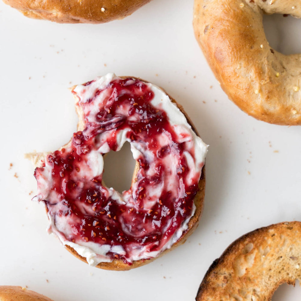 
                  
                    Load image into Gallery viewer, Spread The Love Raspberry Artisan Jam on bagel with cream cheese
                  
                